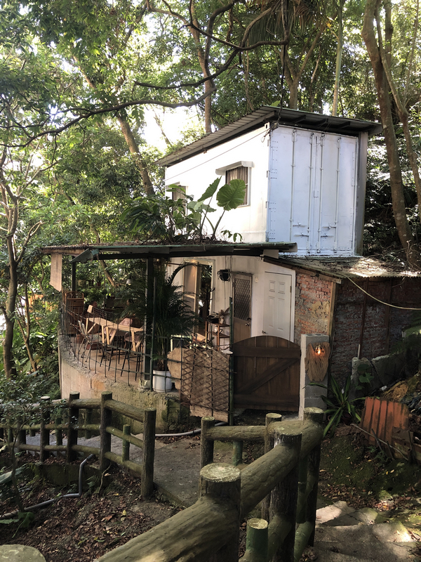 渡深咖啡廳外觀，位於深坑山林中的秘境空間，融合木材、鐵皮與白牆建築，周圍環繞濃密樹林與石階小徑，展現自然靜謐氛圍。