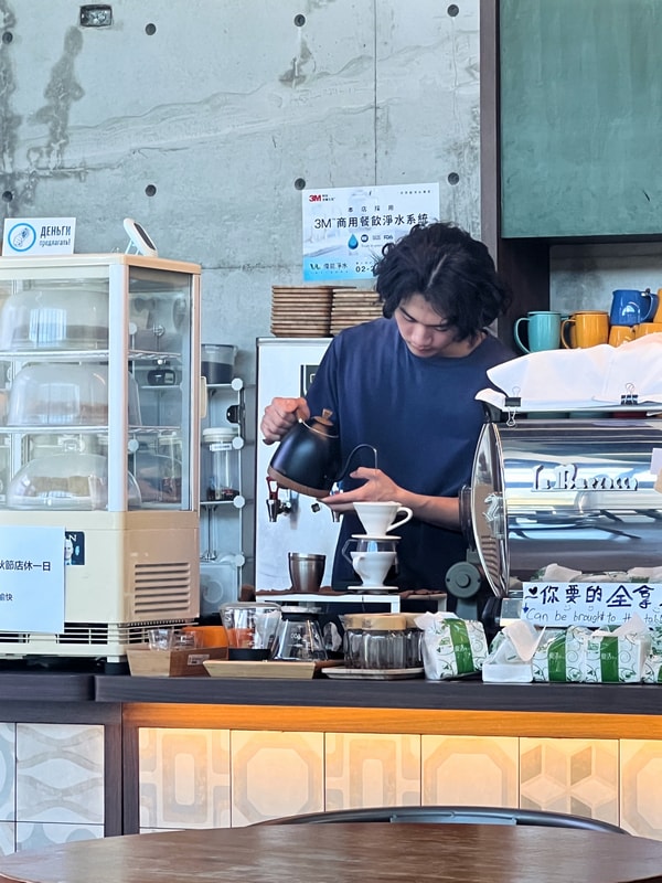 Arc Cafe 手沖咖啡區，Barista 使用細口壺進行手沖，背景為清水模牆面與咖啡器具，營造專注與職人氛圍。