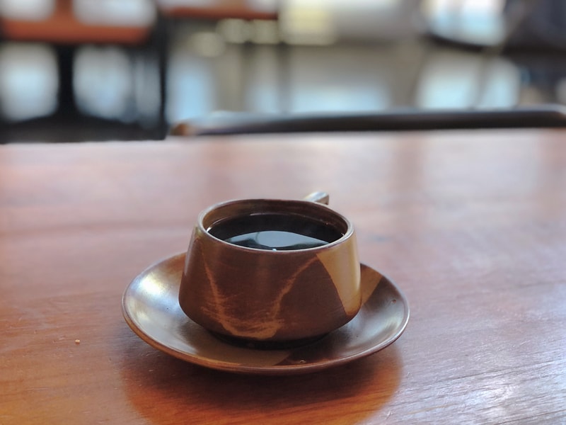 陶杯盛裝深色咖啡，理論上應有茉莉花、柳橙、杏桃等香氣，但實際風味模糊，層次不明。整體略感失望，未能展現預期的花果香旅程。背景溫暖，氛圍療癒。