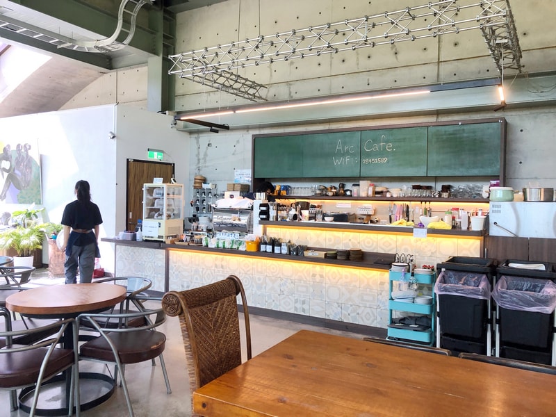 Arc Cafe 櫃檯區域，清水模牆面與綠色手寫黑板構成，空間寬敞明亮，設有兒童座椅與親子友善動線。