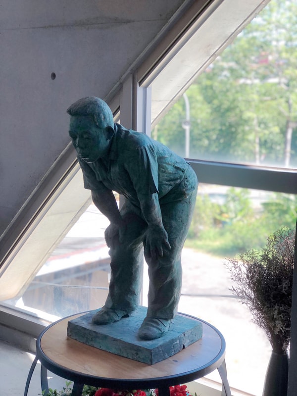 Arc Cafe 二樓角落，一尊彎身撐膝的雕像。營造著靜謐與沉思的氛圍。