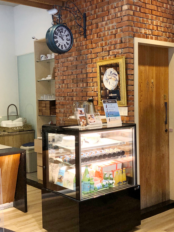 波赫士領地精品咖啡館明水店|台北大直不限時咖啡廳推薦,開心果奶霜千層必吃甜點 - 第16張圖 櫃台上方的磚牆掛盤與復古時鐘,讓整體氛圍多了一份靜謐的時間感。