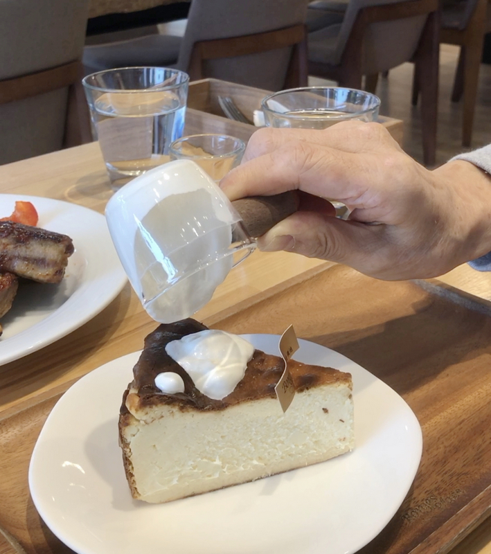 波赫士領地精品咖啡館明水店|台北大直不限時咖啡廳推薦,開心果奶霜千層必吃甜點 - 第27張圖 手持透明杯緩緩倒入奶霜,覆蓋在焦香巴斯克奶酪蛋糕上,呈現療癒的甜點瞬間。